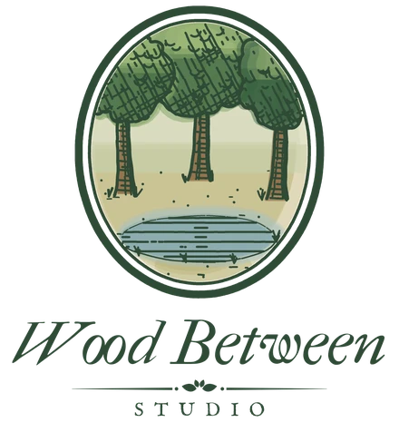 Wood Between Studio logo: three trees beside a small pool, inside an oval frame